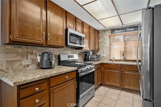 kitchen with appliances with stainless steel finishes, sink, backsplash, light tile patterned flooring, and light stone counters