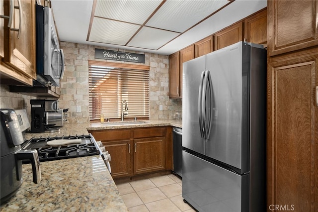 kitchen with appliances with stainless steel finishes, decorative backsplash, sink, light stone counters, and light tile patterned floors