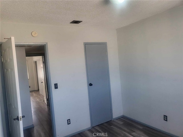 unfurnished bedroom featuring a closet, dark hardwood / wood-style floors, and a textured ceiling