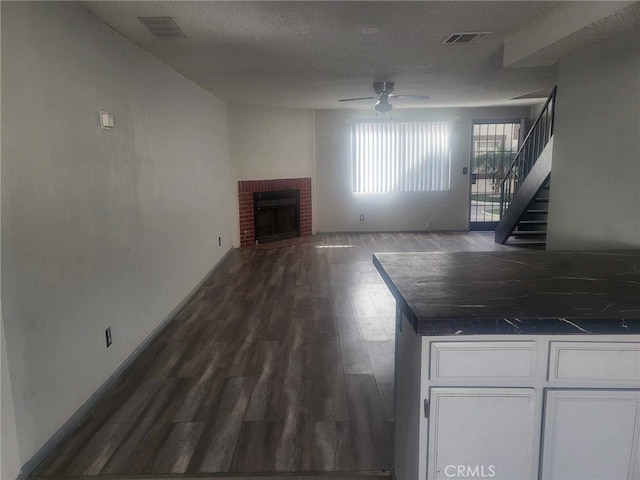 unfurnished living room featuring a brick fireplace, dark hardwood / wood-style floors, a textured ceiling, and ceiling fan