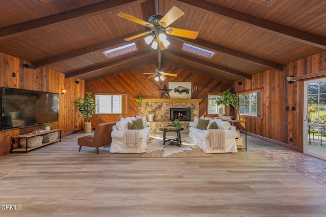 living room featuring a stone fireplace, light wood-type flooring, vaulted ceiling with skylight, and wood ceiling