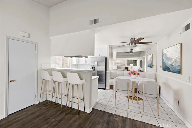 kitchen with a breakfast bar area, stainless steel fridge, white cabinets, kitchen peninsula, and light wood-type flooring