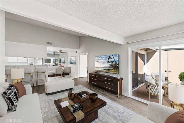 living room featuring ceiling fan, lofted ceiling, a textured ceiling, and light wood-type flooring