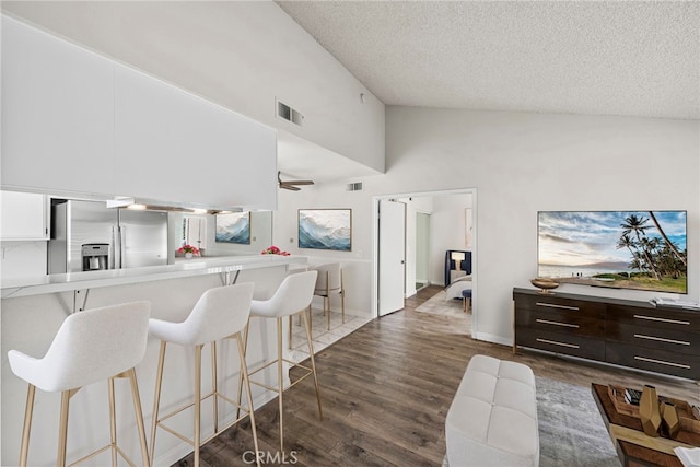 kitchen with white cabinetry, dark brown cabinets, high vaulted ceiling, stainless steel refrigerator with ice dispenser, and a kitchen bar