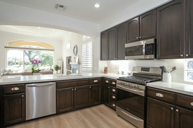 kitchen with appliances with stainless steel finishes, sink, kitchen peninsula, dark brown cabinets, and light wood-type flooring