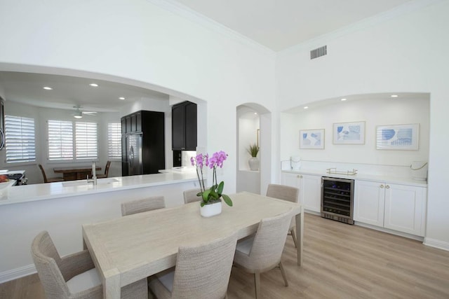 dining room with ornamental molding, beverage cooler, sink, and light hardwood / wood-style flooring