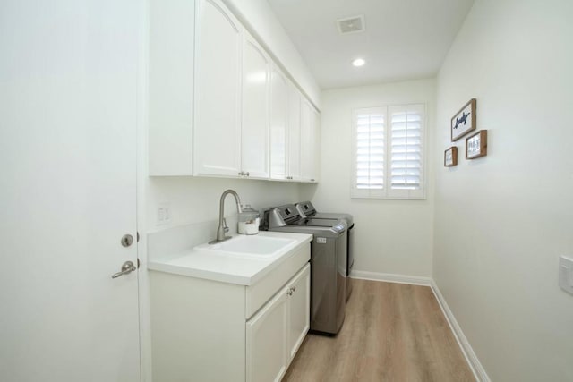 laundry room with cabinets, washer and clothes dryer, sink, and light hardwood / wood-style flooring