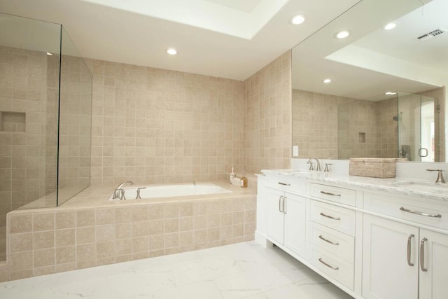 bathroom with vanity, a relaxing tiled tub, and tile walls