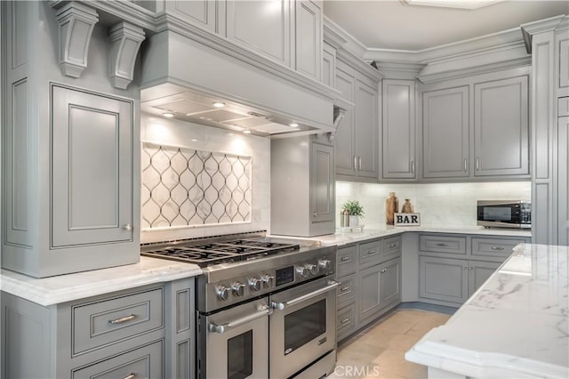 kitchen with tasteful backsplash, premium range hood, gray cabinetry, stainless steel appliances, and light stone counters