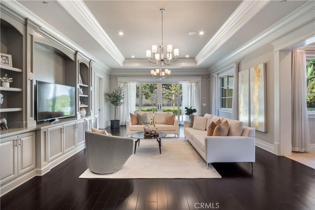 living room featuring built in features, a chandelier, wood-type flooring, and a tray ceiling