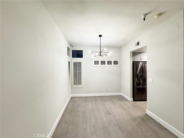 interior space with light wood-type flooring, a textured ceiling, and a notable chandelier