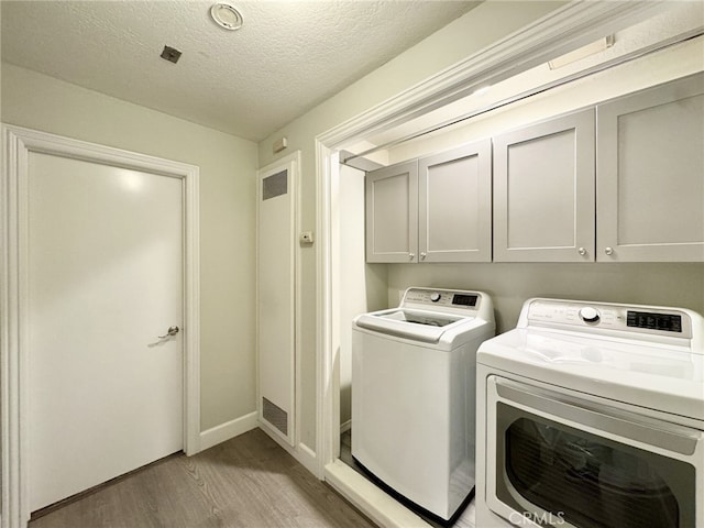 laundry area with washer and dryer, cabinets, a textured ceiling, and light hardwood / wood-style flooring