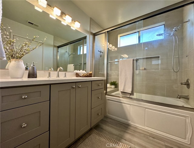 bathroom with wood finished floors, combined bath / shower with glass door, vanity, and visible vents