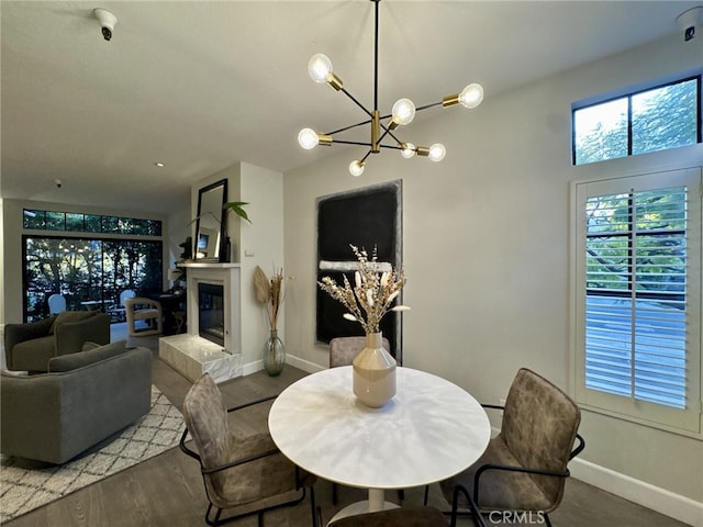 dining space with baseboards, wood finished floors, a notable chandelier, and a glass covered fireplace