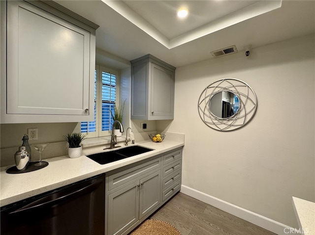 kitchen featuring black dishwasher, gray cabinets, light countertops, a raised ceiling, and a sink