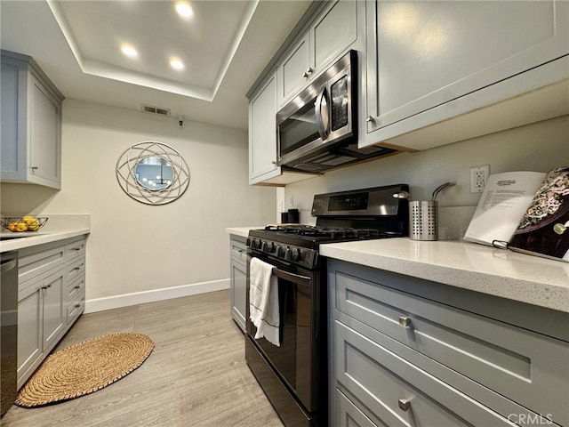 kitchen featuring visible vents, a raised ceiling, appliances with stainless steel finishes, gray cabinets, and light wood-style floors