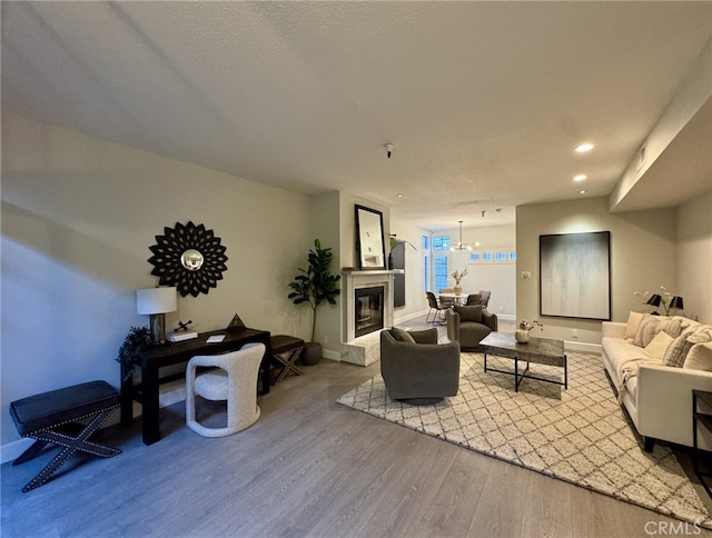 living area with baseboards, a glass covered fireplace, an inviting chandelier, light wood-style floors, and recessed lighting