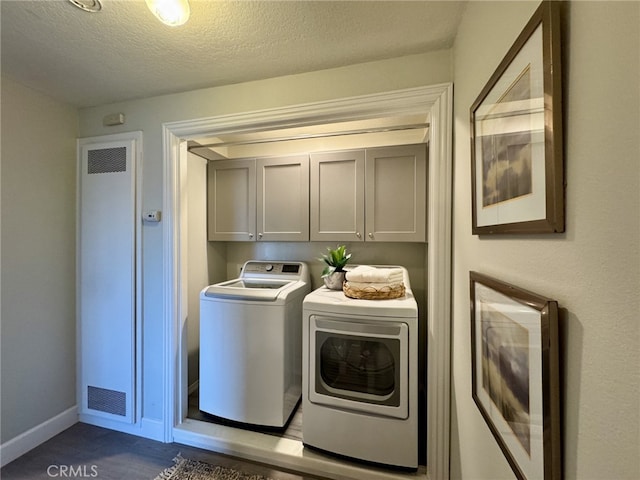 washroom featuring a textured ceiling, washing machine and dryer, visible vents, baseboards, and cabinet space