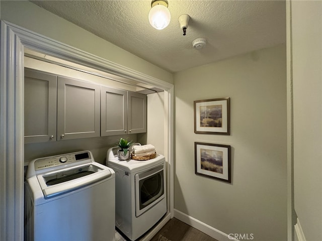 clothes washing area featuring dark wood-style flooring, washer and clothes dryer, cabinet space, a textured ceiling, and baseboards