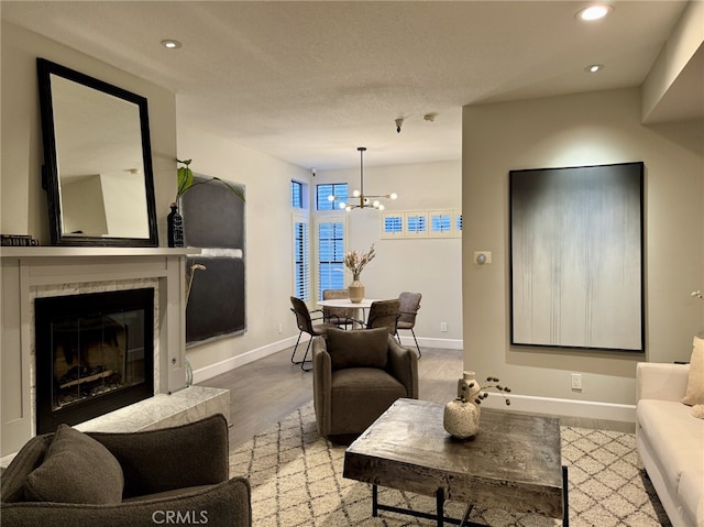 living area featuring light wood finished floors, baseboards, a notable chandelier, and a glass covered fireplace