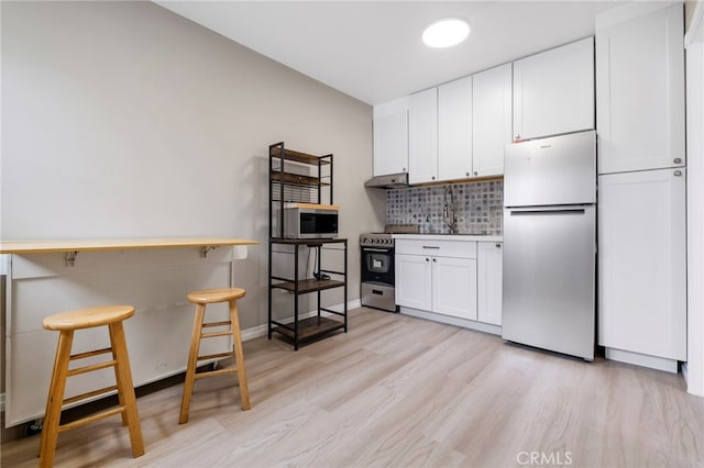 kitchen with white cabinetry, decorative backsplash, light hardwood / wood-style flooring, stainless steel appliances, and a breakfast bar area