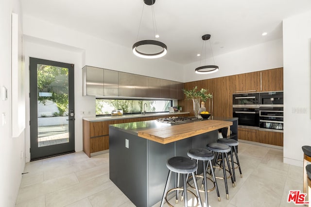 kitchen featuring a kitchen bar, sink, butcher block countertops, decorative light fixtures, and a kitchen island