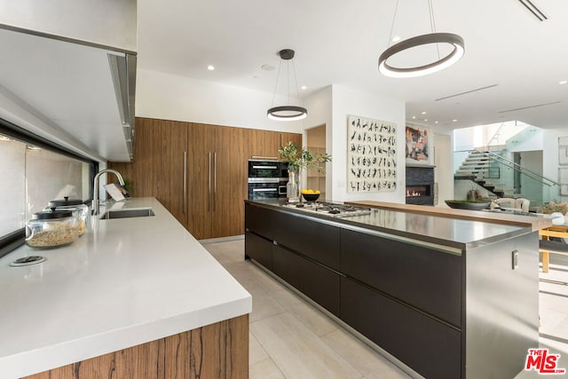 kitchen with pendant lighting, wood walls, stainless steel gas stovetop, sink, and a large island