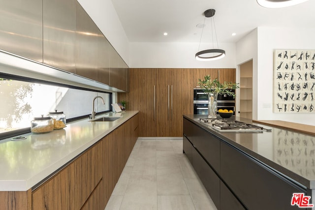 kitchen featuring double oven, stainless steel gas stovetop, decorative light fixtures, and sink