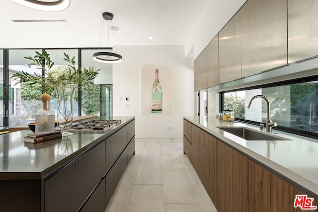 kitchen with stainless steel gas stovetop, light tile patterned flooring, sink, and decorative light fixtures