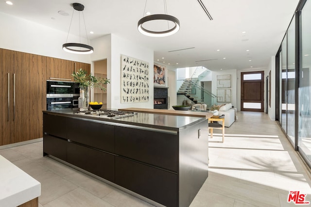 kitchen featuring pendant lighting, double oven, stainless steel gas cooktop, expansive windows, and wood walls