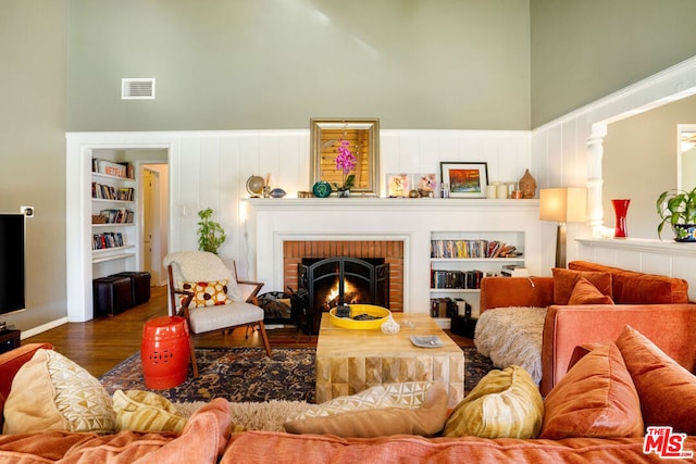 living room featuring a brick fireplace, dark wood-type flooring, built in features, and a high ceiling