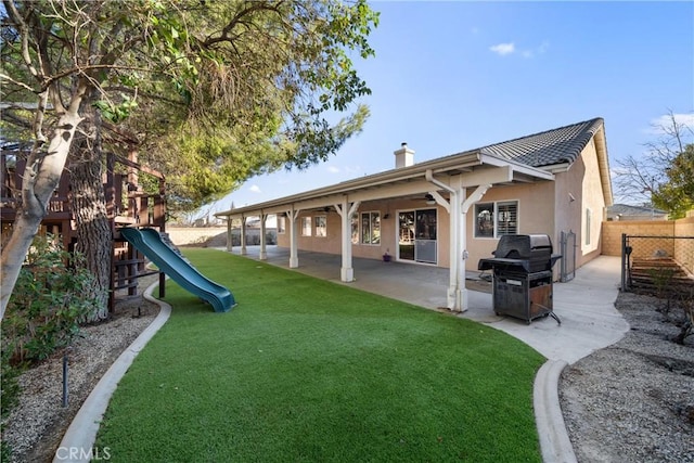 rear view of house featuring a playground, a lawn, and a patio