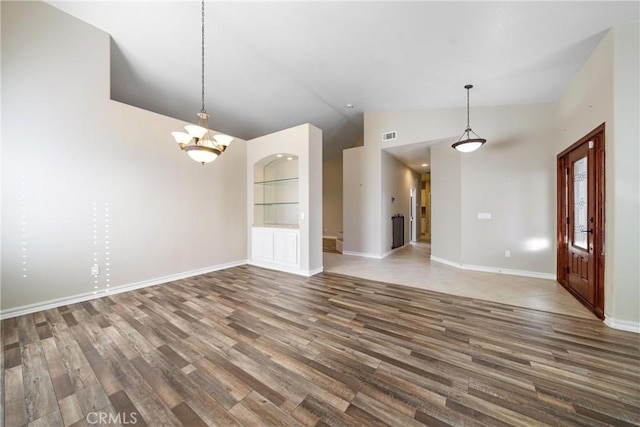 unfurnished living room with built in features, vaulted ceiling, a notable chandelier, and dark hardwood / wood-style floors