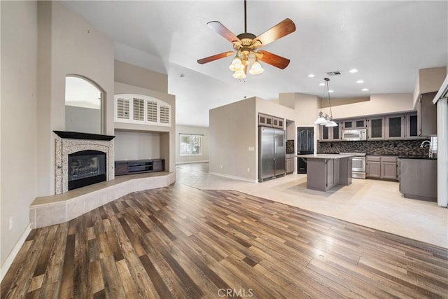 kitchen featuring appliances with stainless steel finishes, decorative light fixtures, gray cabinets, a center island, and decorative backsplash