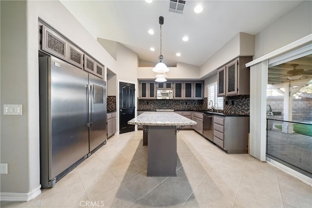 kitchen featuring vaulted ceiling, appliances with stainless steel finishes, decorative light fixtures, dark stone counters, and a kitchen island