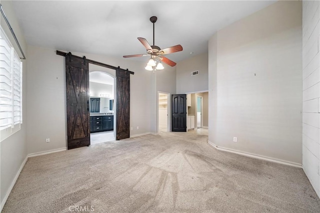 unfurnished bedroom featuring ceiling fan, ensuite bath, a barn door, light carpet, and vaulted ceiling