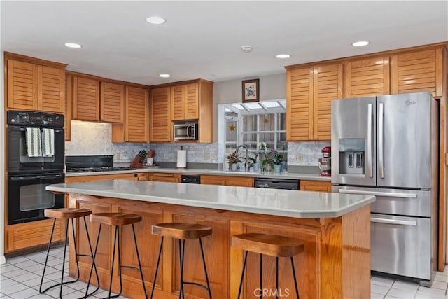 kitchen with a kitchen island, light tile patterned flooring, black appliances, and a kitchen bar