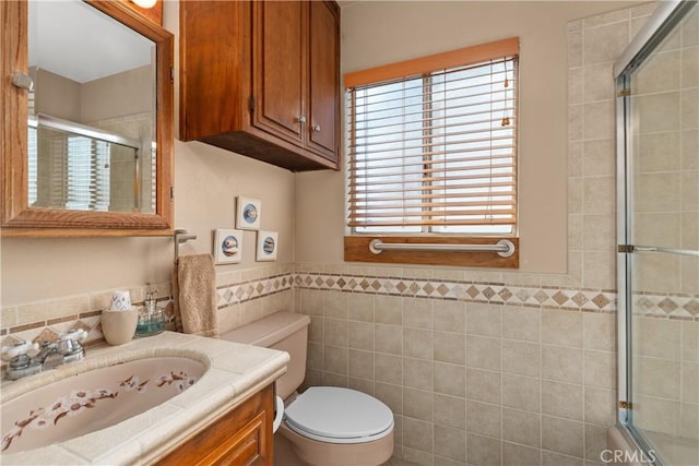 bathroom with tile walls, an enclosed shower, vanity, and toilet