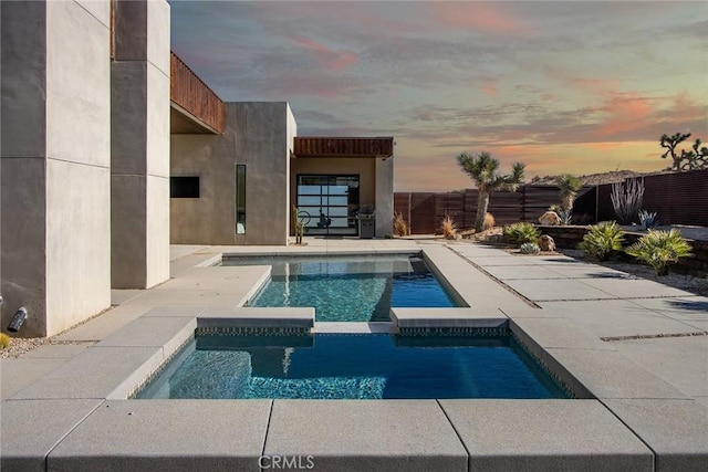 pool at dusk featuring an in ground hot tub and a patio