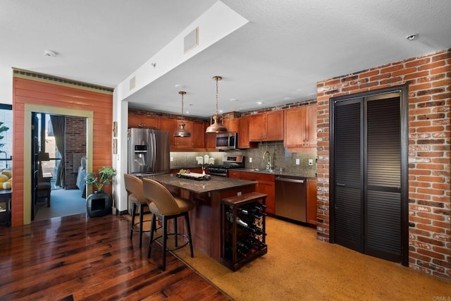 kitchen with sink, appliances with stainless steel finishes, hanging light fixtures, a kitchen island, and decorative backsplash