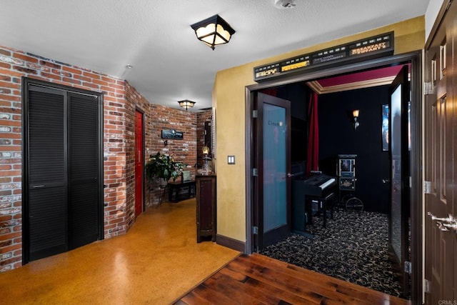 hall featuring brick wall, light hardwood / wood-style floors, and a textured ceiling