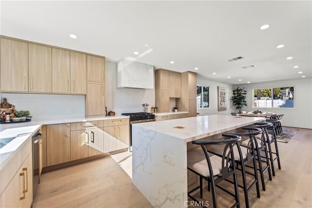 kitchen with a center island, light stone countertops, appliances with stainless steel finishes, a breakfast bar area, and light brown cabinets