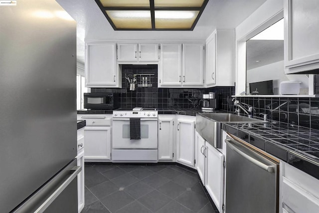 kitchen with dark tile patterned flooring, white cabinets, appliances with stainless steel finishes, sink, and backsplash