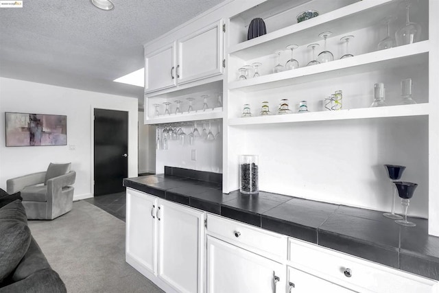 kitchen with white cabinetry, a textured ceiling, tile counters, and light carpet