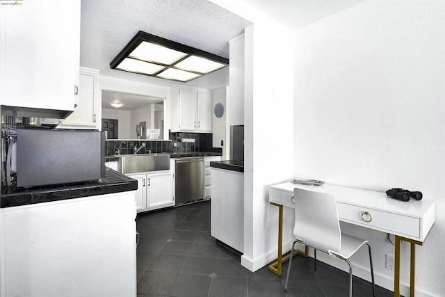 kitchen with stainless steel dishwasher, dark tile patterned floors, sink, white cabinets, and tasteful backsplash