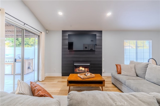 living room featuring plenty of natural light, a large fireplace, lofted ceiling, and light wood-type flooring