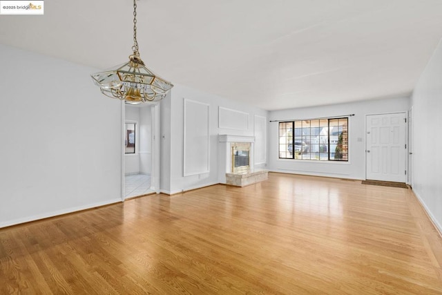 unfurnished living room featuring a premium fireplace, a chandelier, and light wood-type flooring