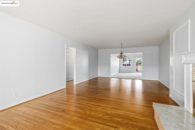 empty room with a tiled fireplace, light hardwood / wood-style flooring, and an inviting chandelier