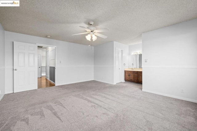 unfurnished bedroom with connected bathroom, a textured ceiling, light colored carpet, and ceiling fan