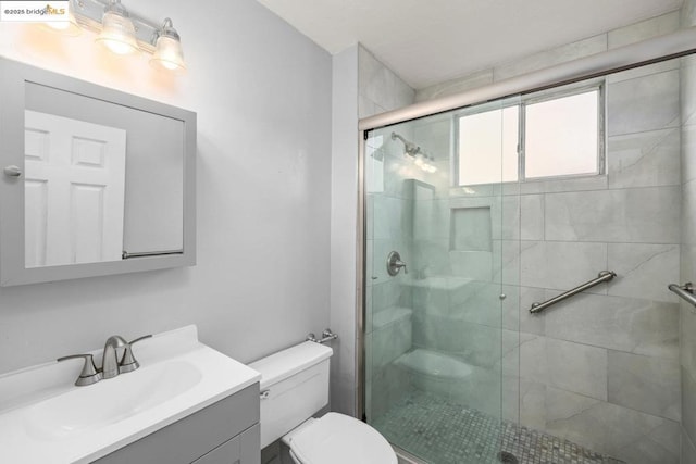 bathroom featuring a shower with door, vanity, and toilet